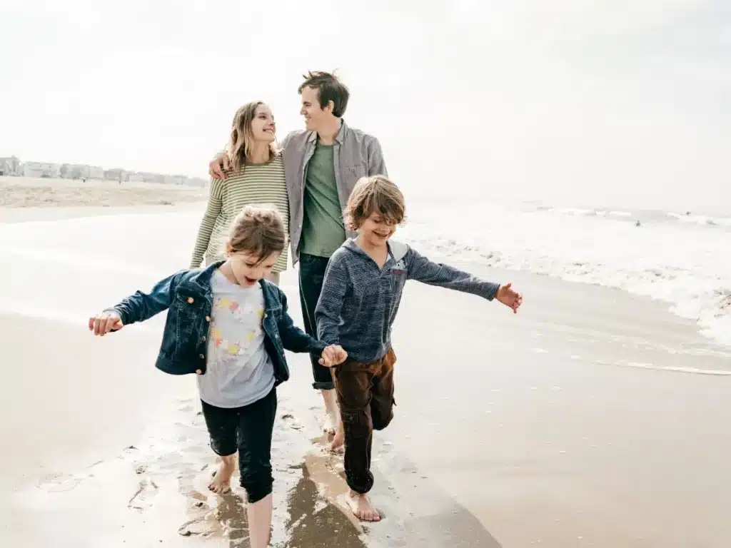 Familia feliz con dos niños caminando descalzos por la orilla de una playa, disfrutando del mar.